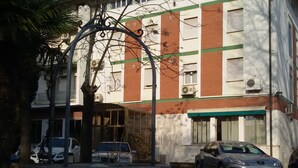 Un edificio con una estructura circular de piedra al frente, coches aparcados y cielo despejado.