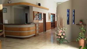 Zona de recepción con mostrador de madera, un tablón de anuncios y un arreglo floral.