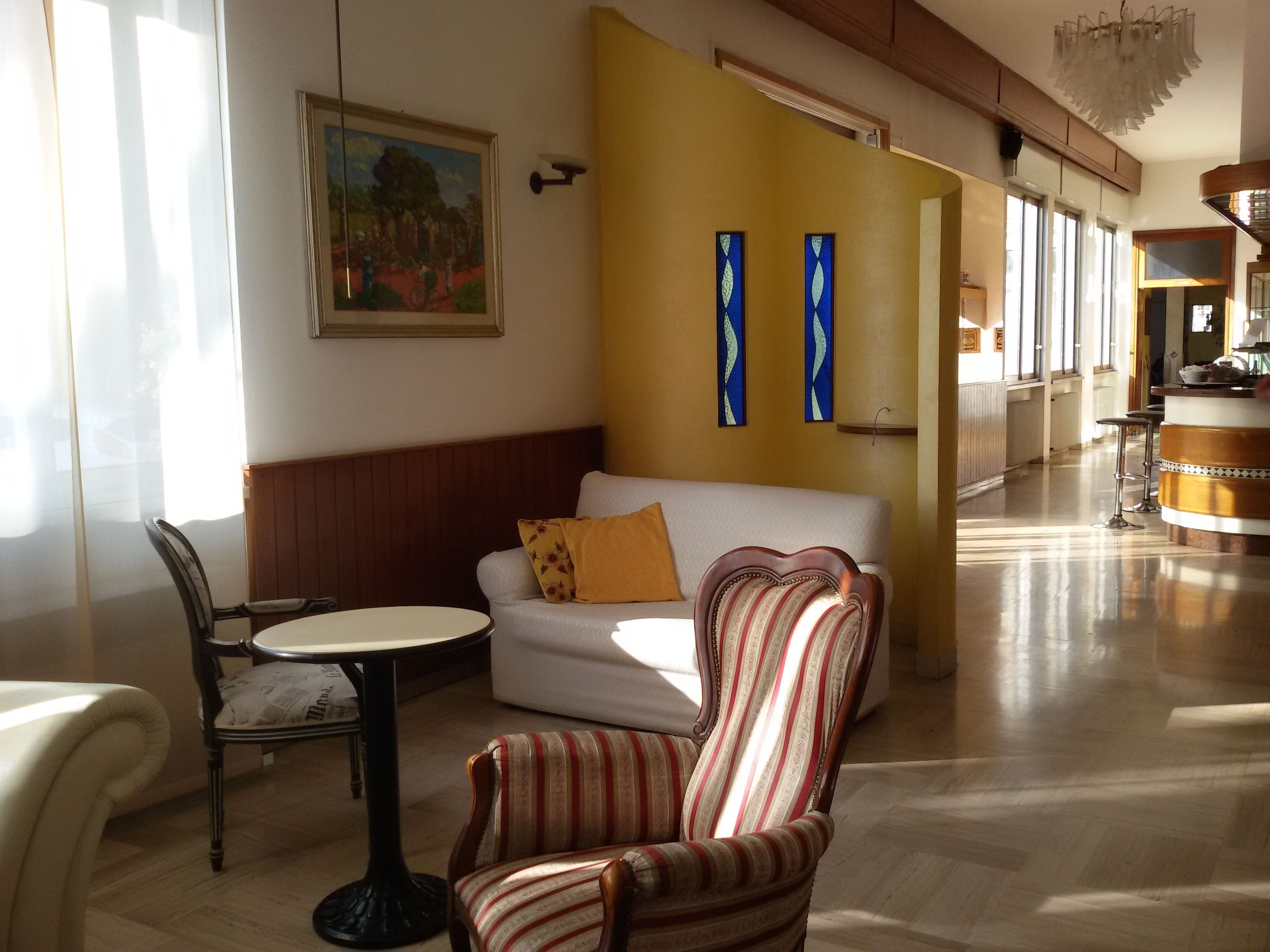 Un hall de hotel con un sofá blanco, un sillón a rayas y una pequeña mesa redonda. Hay dos obras de arte abstractas en la pared, un cuadro sobre el sofá y una araña.