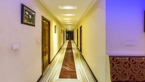 A hotel hallway with a marble floor, framed pictures on the walls, and doors on both sides. - Hotel de Marina (Port Blair)