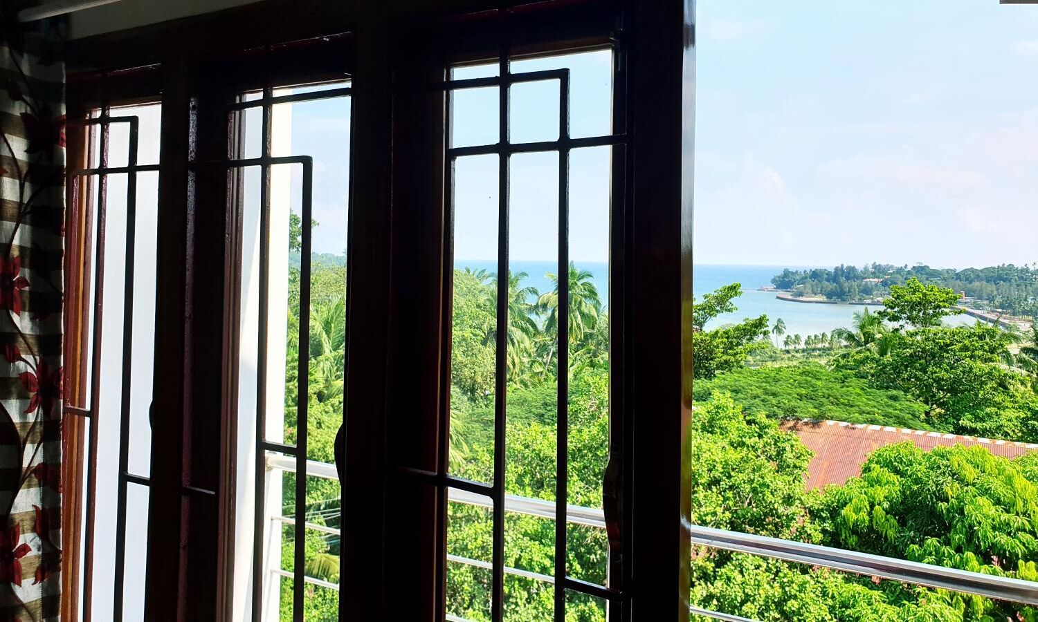 A view from a window with metal bars, overlooking a lush green landscape with a body of water and distant hills.