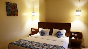 A hotel room with a large bed, two bedside tables, a nightstand, a decorative painting on the wall, and a logo for 'de marina hotels & resorts'. - Hotel de Marina (Port Blair)