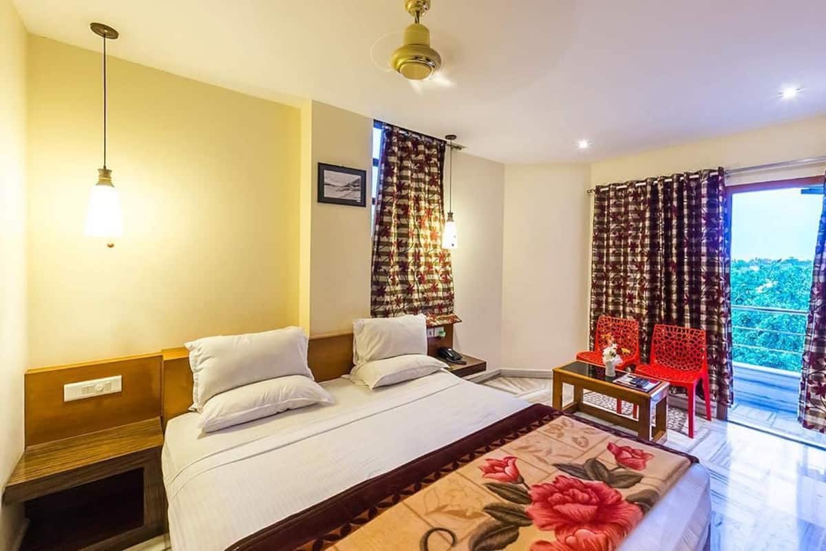 Une chambre d’hôtel comprenant un lit, une table de chevet, un bureau avec une chaise et une fenêtre avec des rideaux.