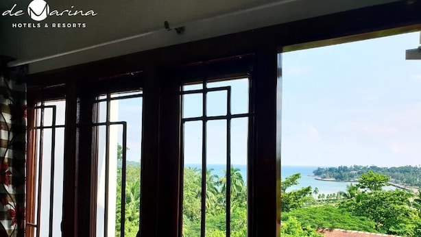 A room with large windows offering a view of a lush landscape and a body of water. - Hotel de Marina (Port Blair)
