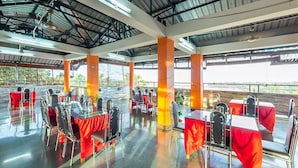 A spacious indoor area with tables and chairs arranged for dining, large pillars, and a high ceiling with visible beams. - Hotel de Marina (Port Blair)