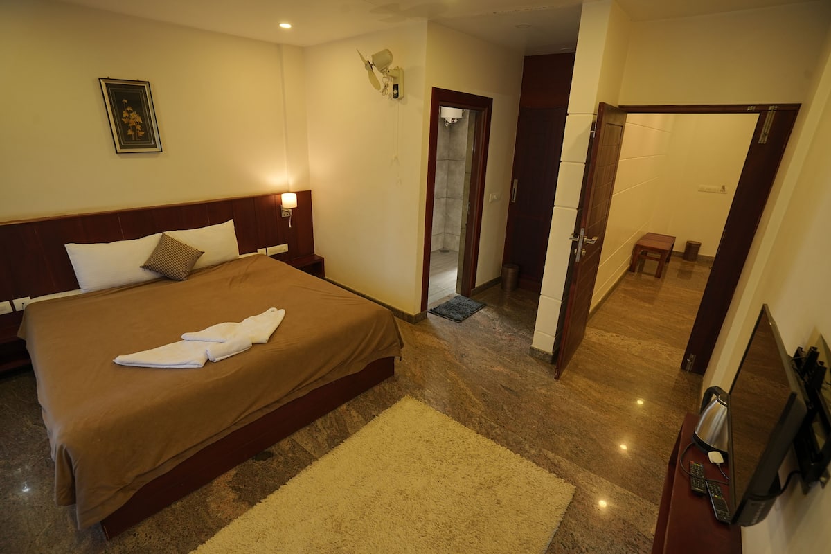 A hotel room with a large bed, a bedside table with a lamp, a wall-mounted TV, and a door leading to a bathroom.