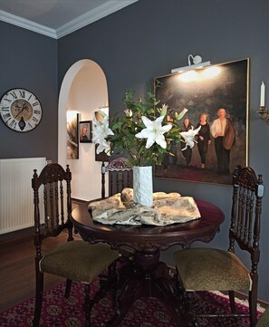 A dining area with a round table, two chairs, a vase with flowers, a clock, and a painting on the wall. - Tiepolo Galleria Palatina (Thessaloniki)