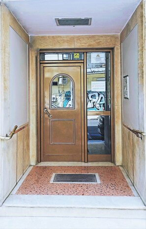 A wooden double door with a glass panel, a doormat, and a metal vent above. - Tiepolo Galleria Palatina (Thessaloniki)