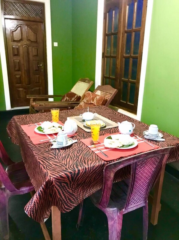 A dining area with a table set for four, including plates, cups, and a glass of orange juice. There are two chairs and a bench.