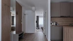 A modern hotel room with a wooden wardrobe, a built-in bench, a kitchenette with a sink and stove, and a large mirror. - Aparthotel Cosy (Stuttgart)