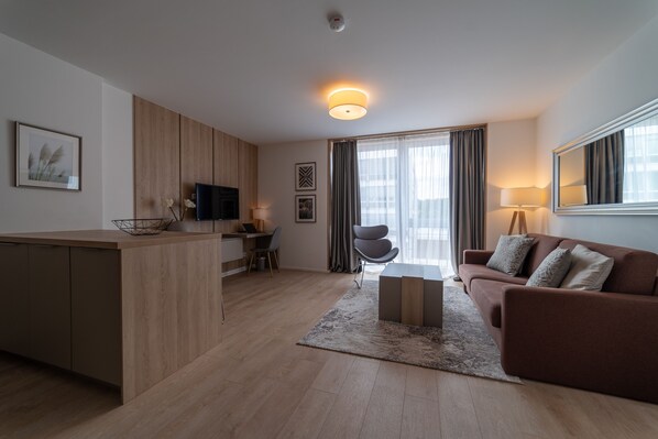 Una sala de estar moderna con un sofá, una mesa de centro, un televisor y un área de cocina con una mesa de comedor y sillas.