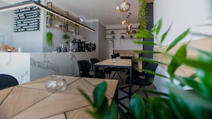 A modern cafe with wooden tables and black chairs, a menu board, and hanging plants. - Aparthotel Cosy (Stuttgart)