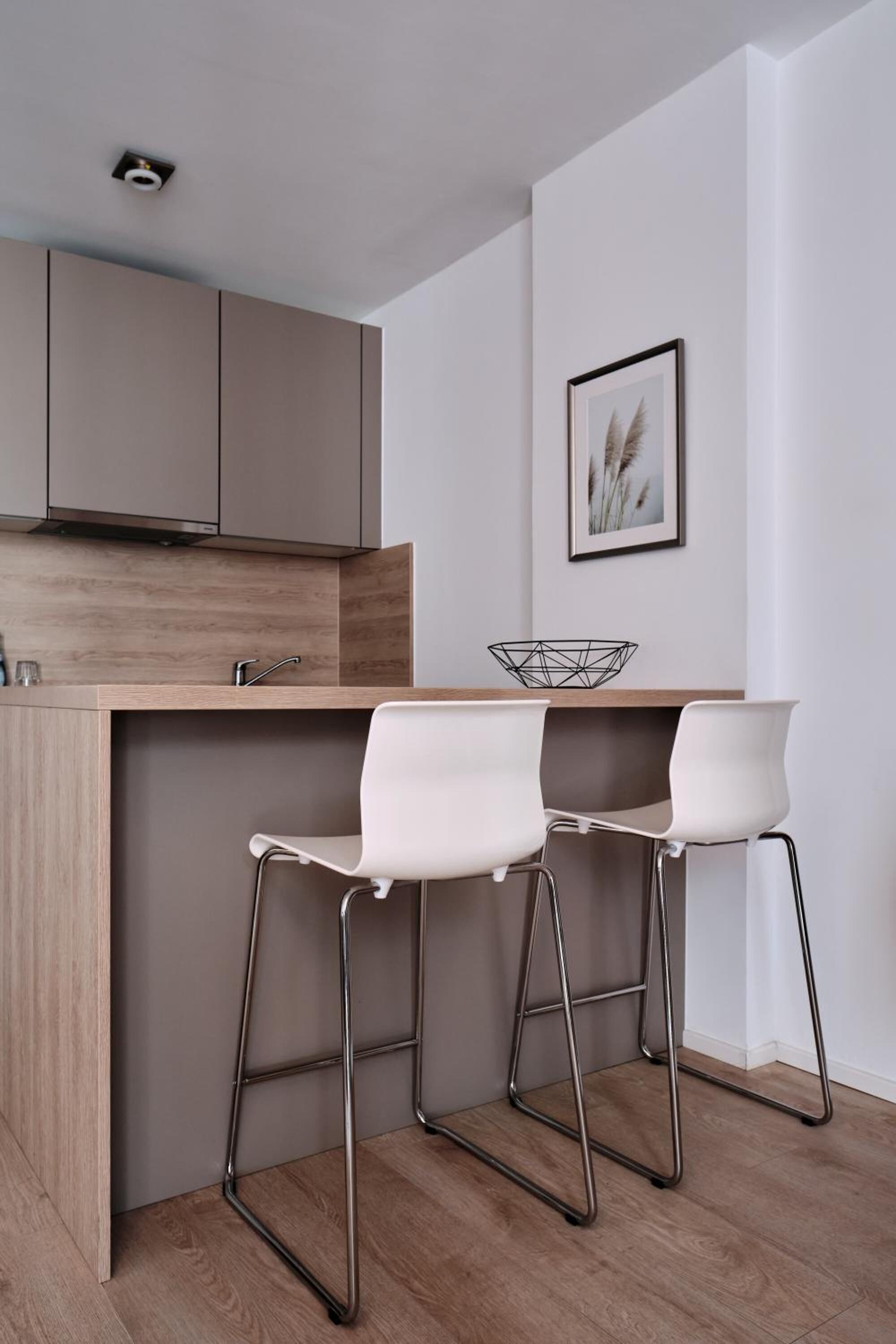 Una cocina moderna con encimera de madera, dos taburetes blancos y un cuadro en la pared.