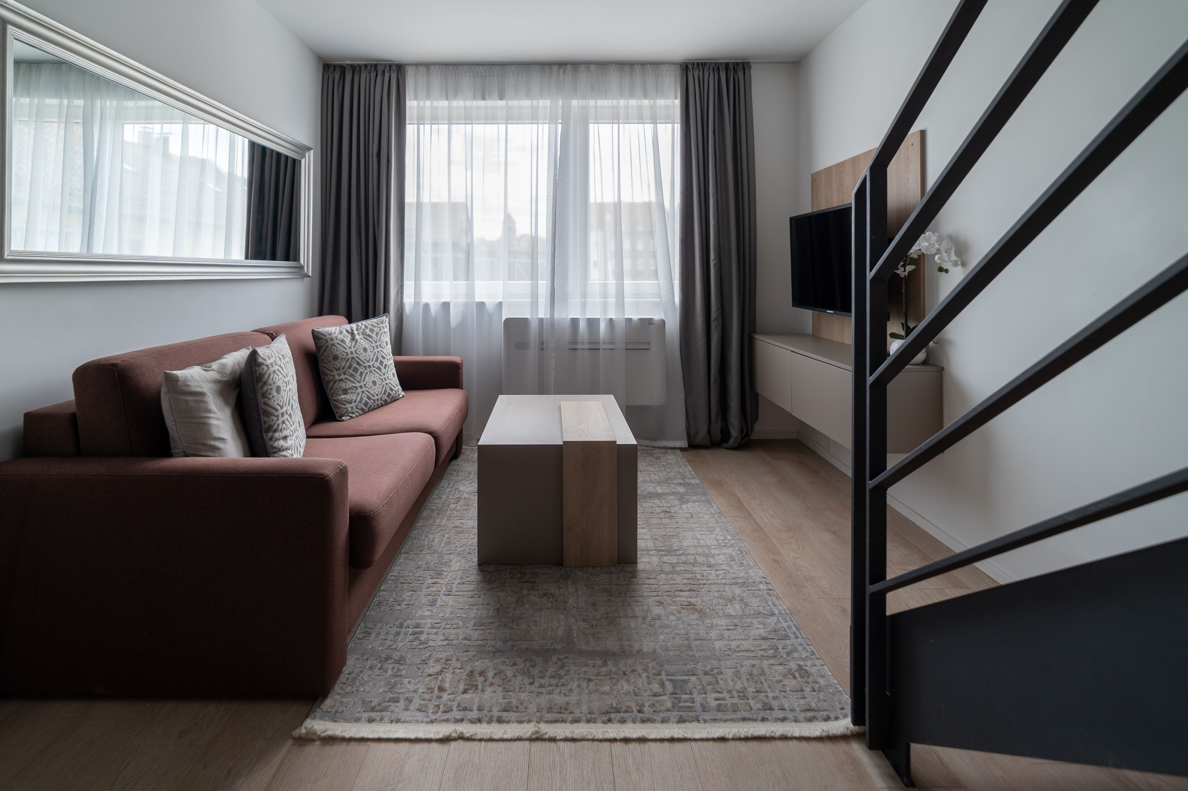 A modern living room with a red sofa, a coffee table, and a staircase.