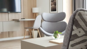 A modern living room with a grey sofa, a small table with a plant, and a flat-screen TV mounted on the wall. - Aparthotel Cosy (Stuttgart)