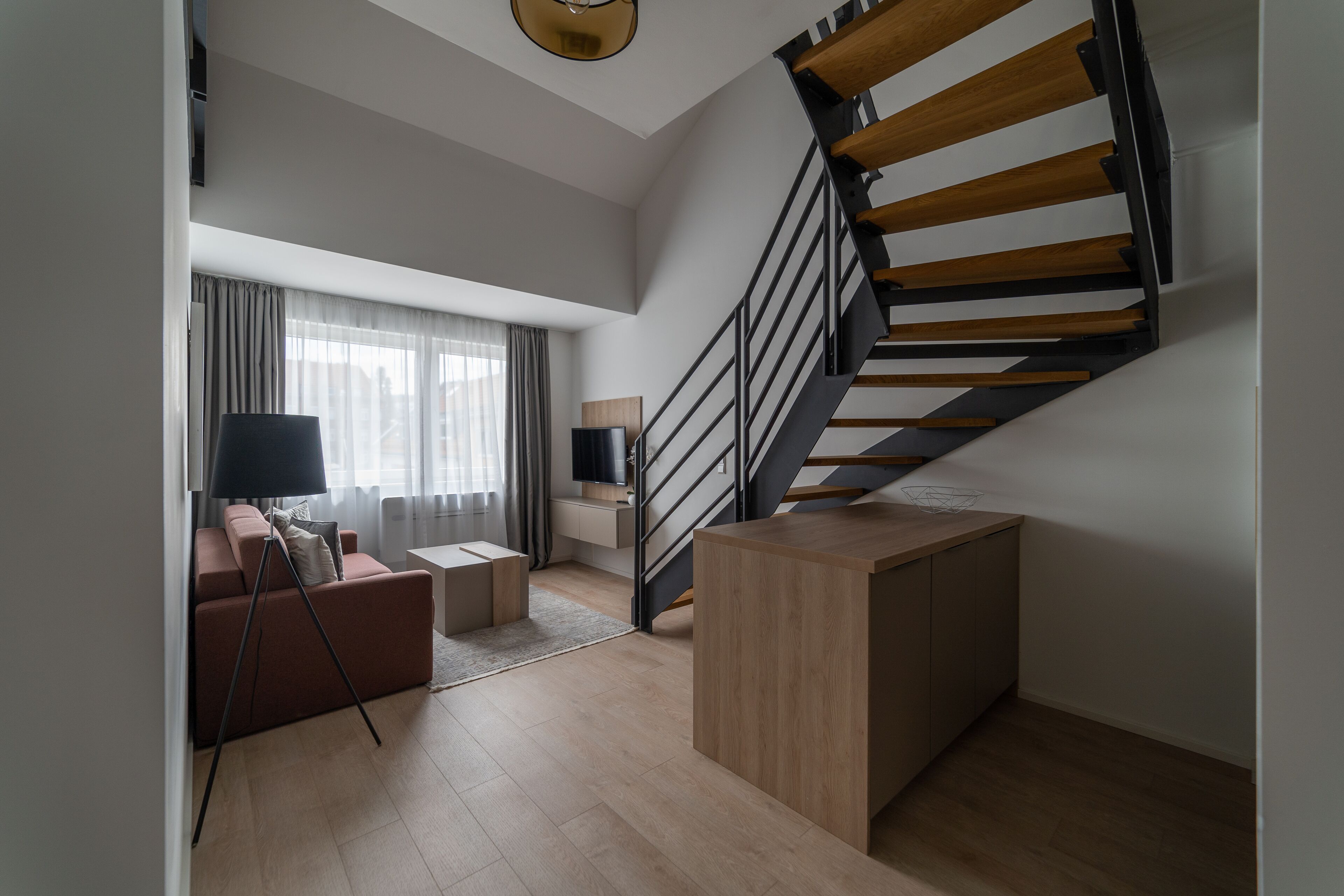 A modern living room with a staircase, a sofa, a coffee table, and a lamp.
