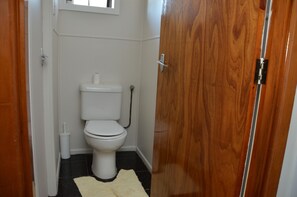 Un baño pequeño con un inodoro, una puerta de madera y un tapete blanco en el suelo.