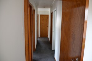 Un pasillo estrecho con puertas de madera a ambos lados, que conduce a una puerta central al final.