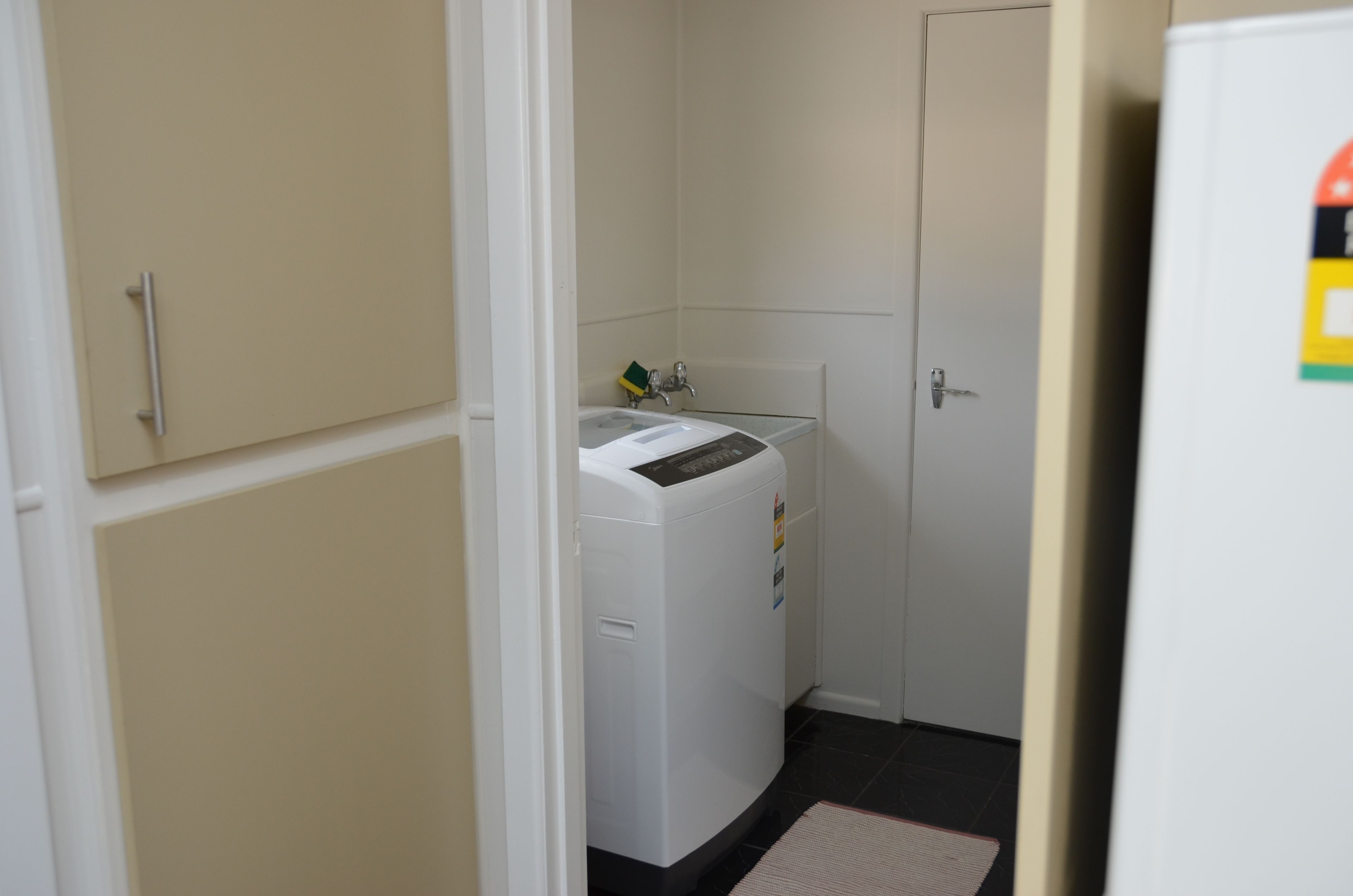 Een wasserette met een wasmachine, een klein keukentje en een deur.