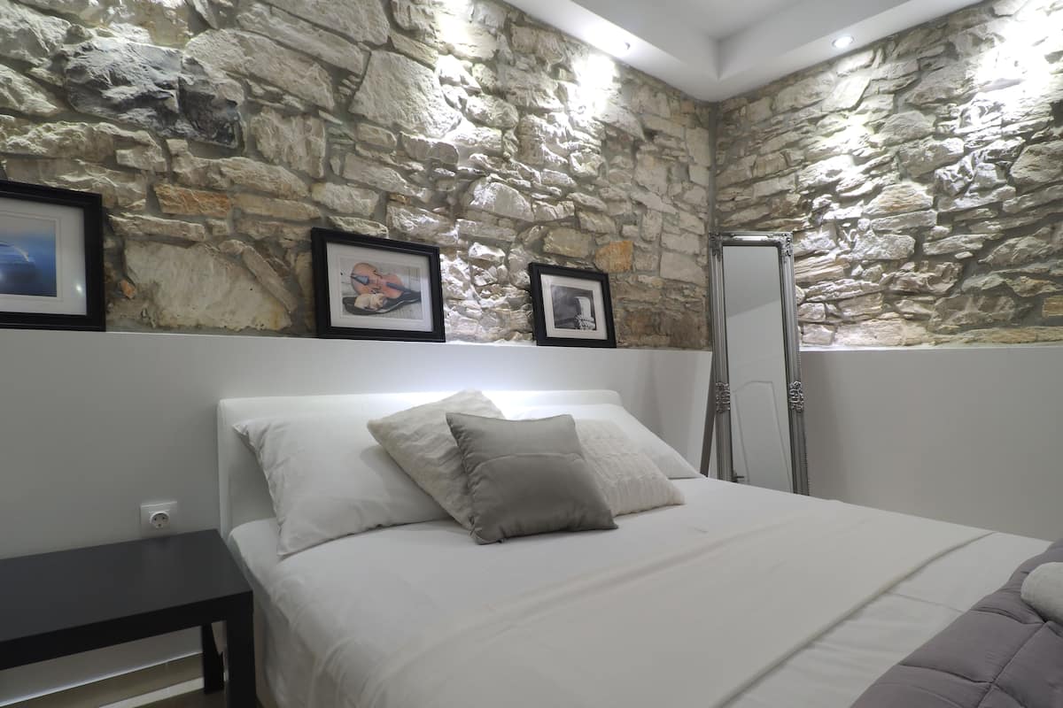 A bedroom with a stone wall, a bed with white bedding, a dark bedside table, and a framed picture on the wall.