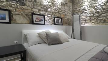 A bedroom with a stone wall, a bed with white bedding, a dark bedside table, and a framed picture on the wall.