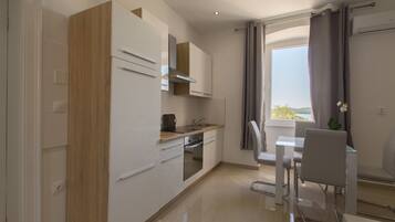 A modern kitchen with white cabinetry, a built-in oven, and a dining area with a glass table and white chairs.