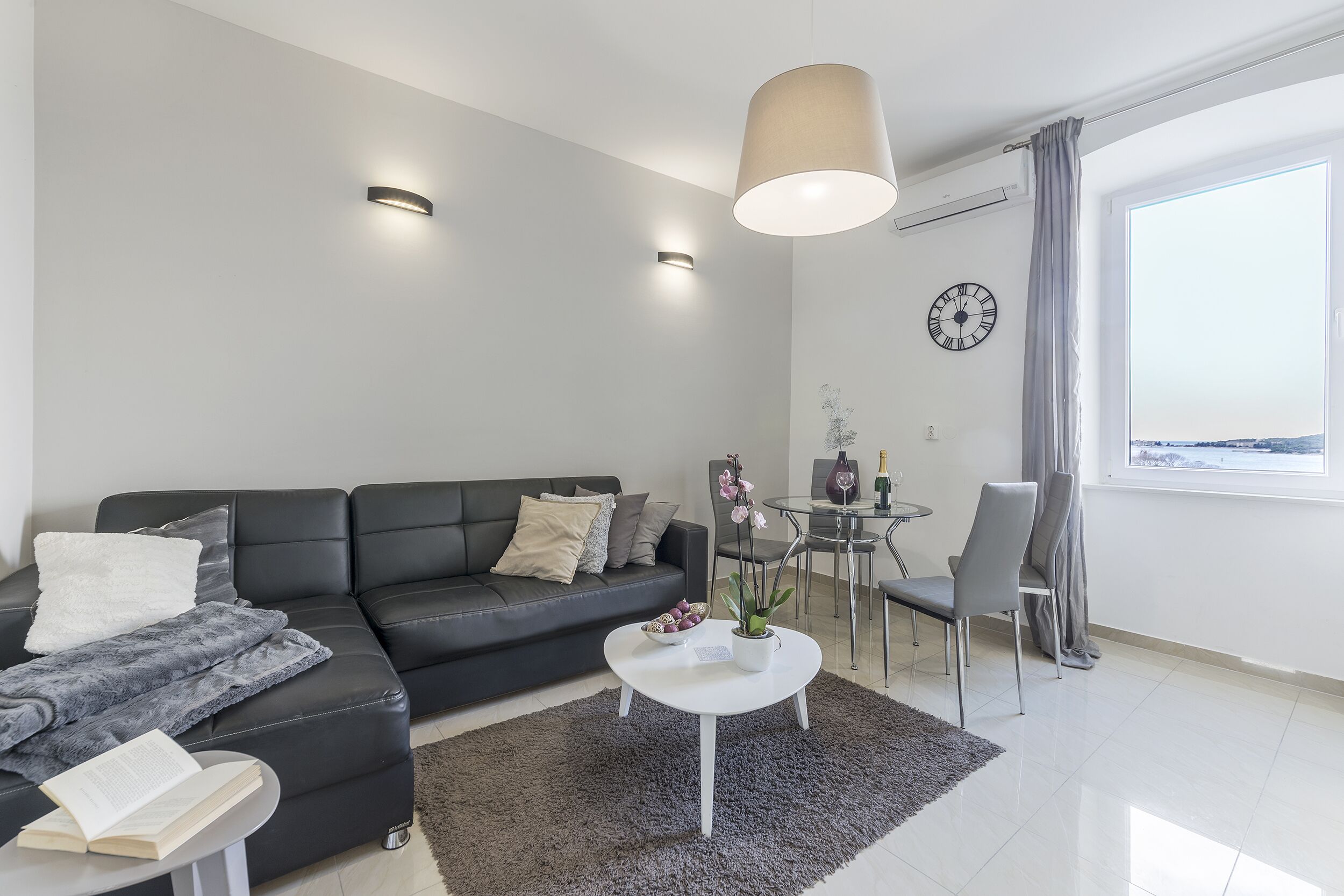 Una sala de estar moderna con un sofá de cuero negro, una mesa de centro blanca y un comedor con una mesa y sillas de vidrio.