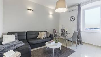 Una sala de estar moderna con un sofá de cuero negro, una mesa de centro blanca y un comedor con una mesa y sillas de vidrio.