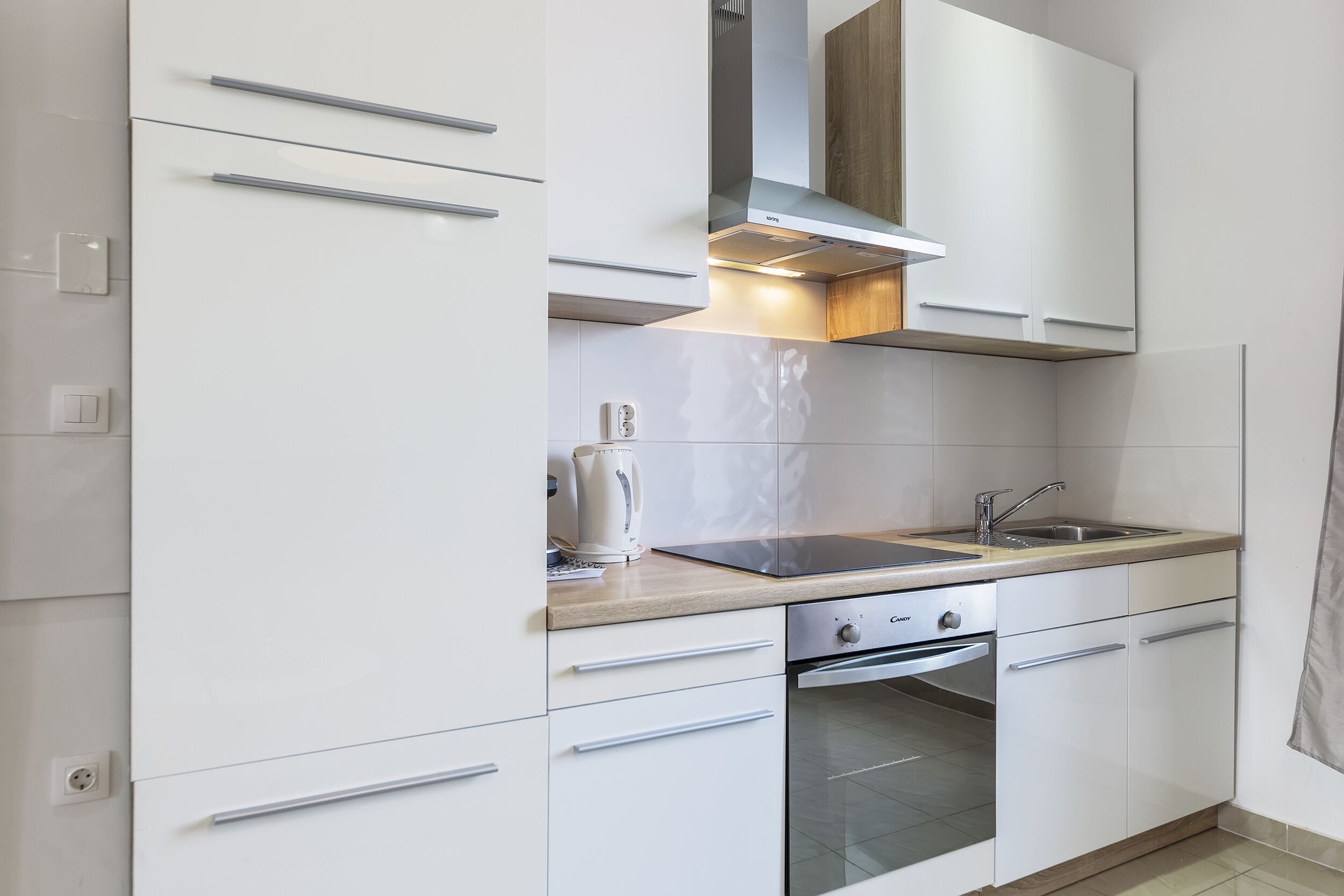 Una cocina moderna con armarios blancos, un lavamanos de acero inoxidable y un horno empotrado.