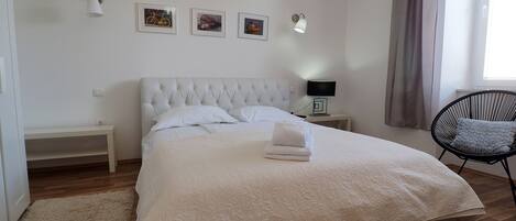 A neatly made bed with a white duvet, a bedside table with a lamp, a chair, and three framed pictures on the wall.
