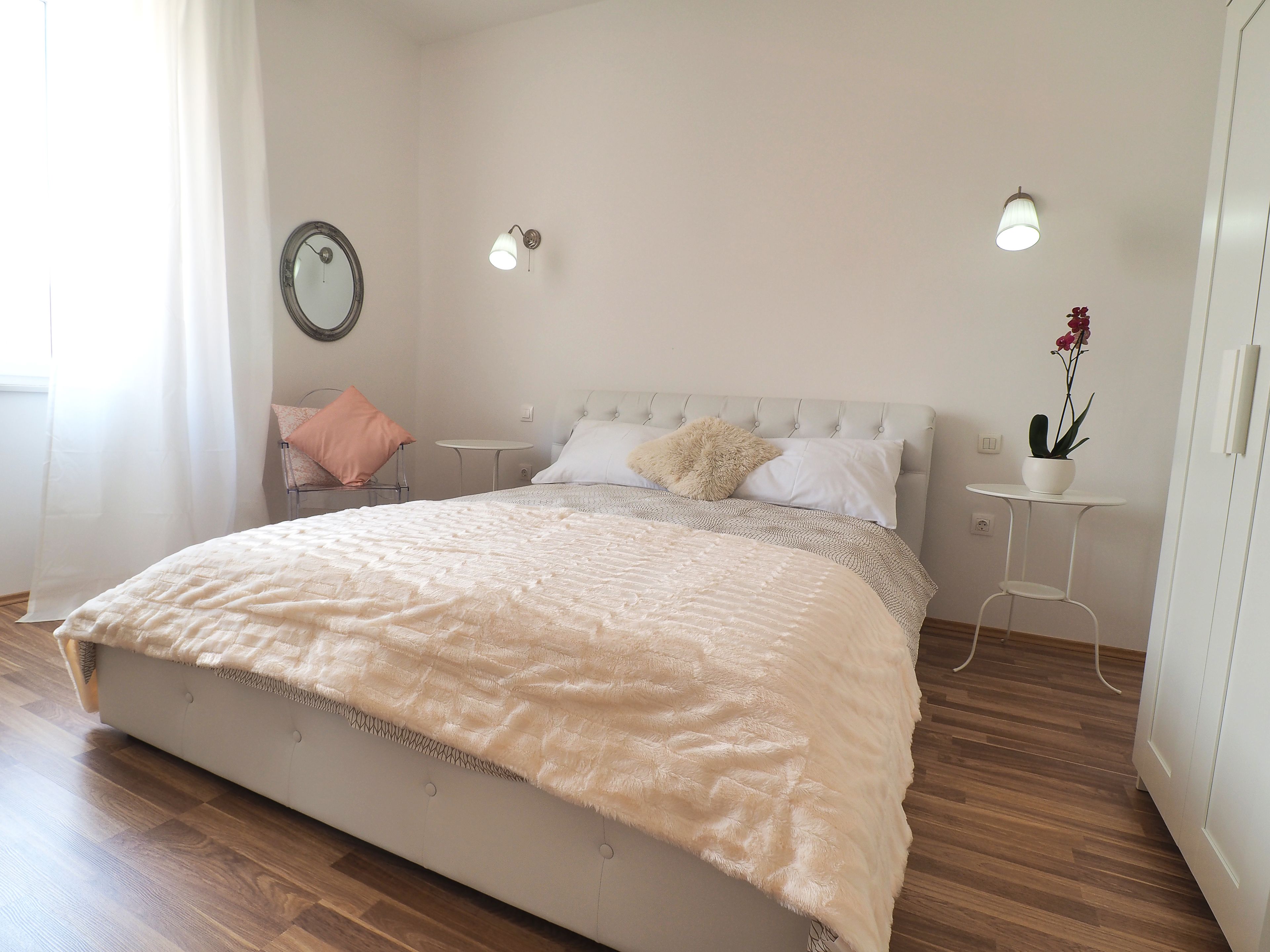 Een keurig opgemaakte slaapkamer met een bed, nachtkastjes, een spiegel en een potplant.