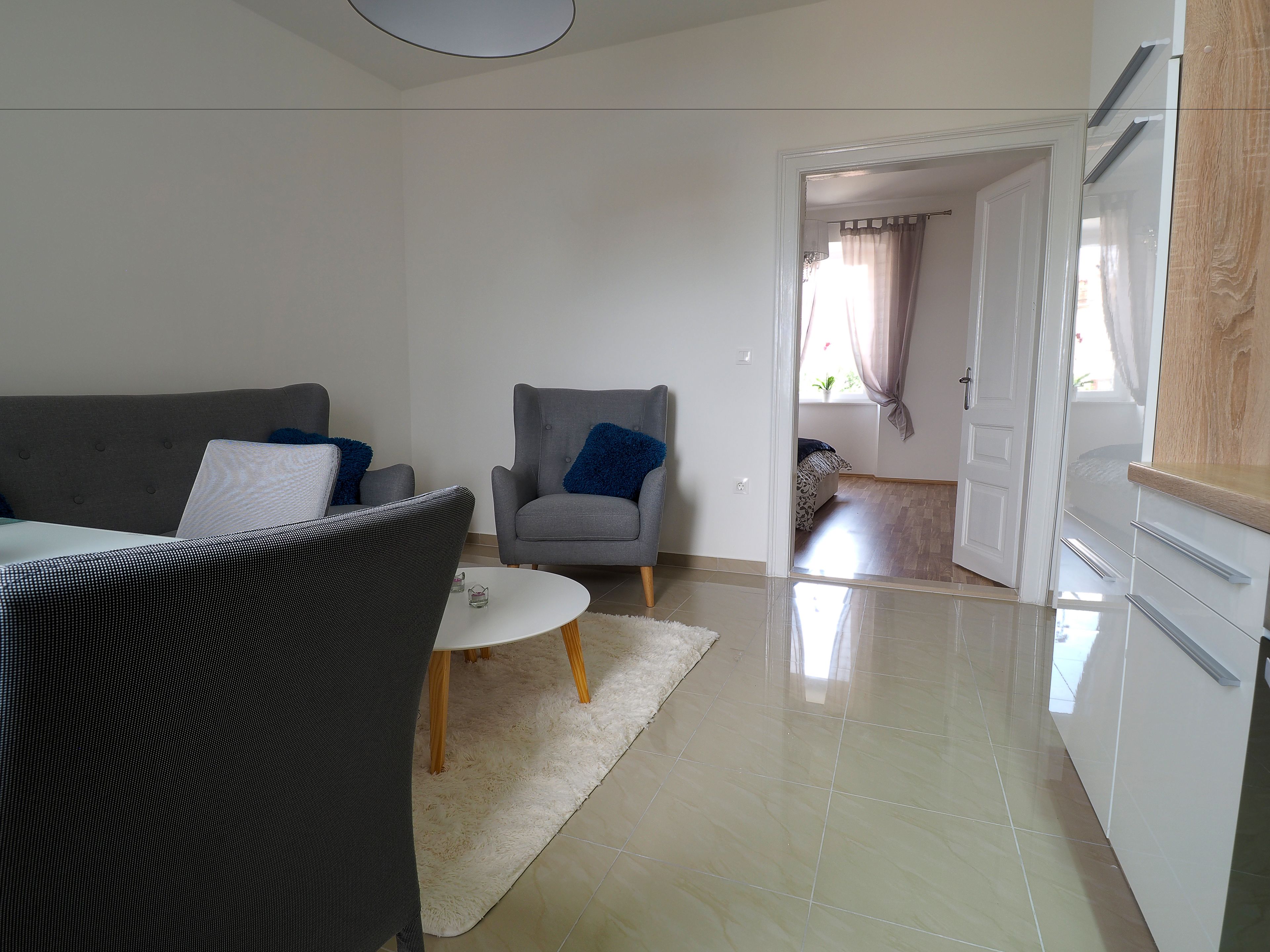A living room with a grey sofa, a grey armchair, and a small white table.