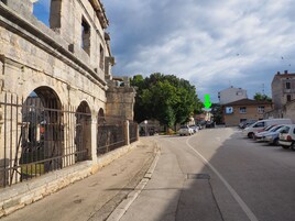 Ένας δρόμος με ένα ιστορικό κτίριο από πέτρα, το οποίο διαθέτει αψίδες και μια πύλη στην είσοδο.