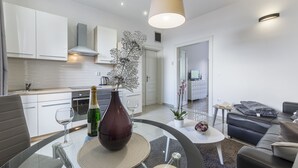 Una cocina moderna con armarios blancos, un comedor con mesa de vidrio y una sala de estar con sofá de cuero negro.