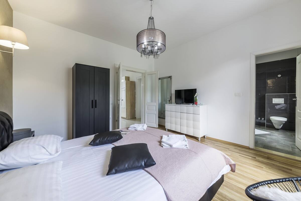 A modern hotel room with a large bed, a wardrobe, a vanity with a mirror, and a bathroom visible through an open door.
