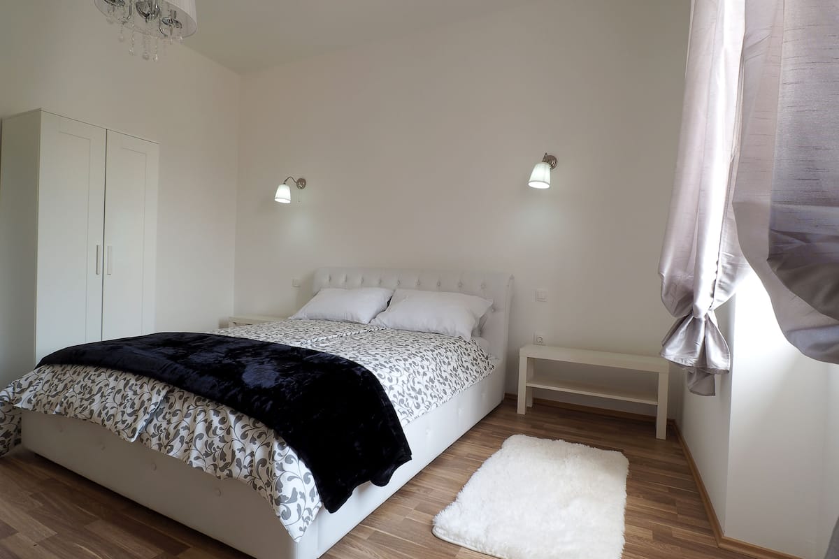 A bedroom with a bed, bedside table, wardrobe, and a white rug.