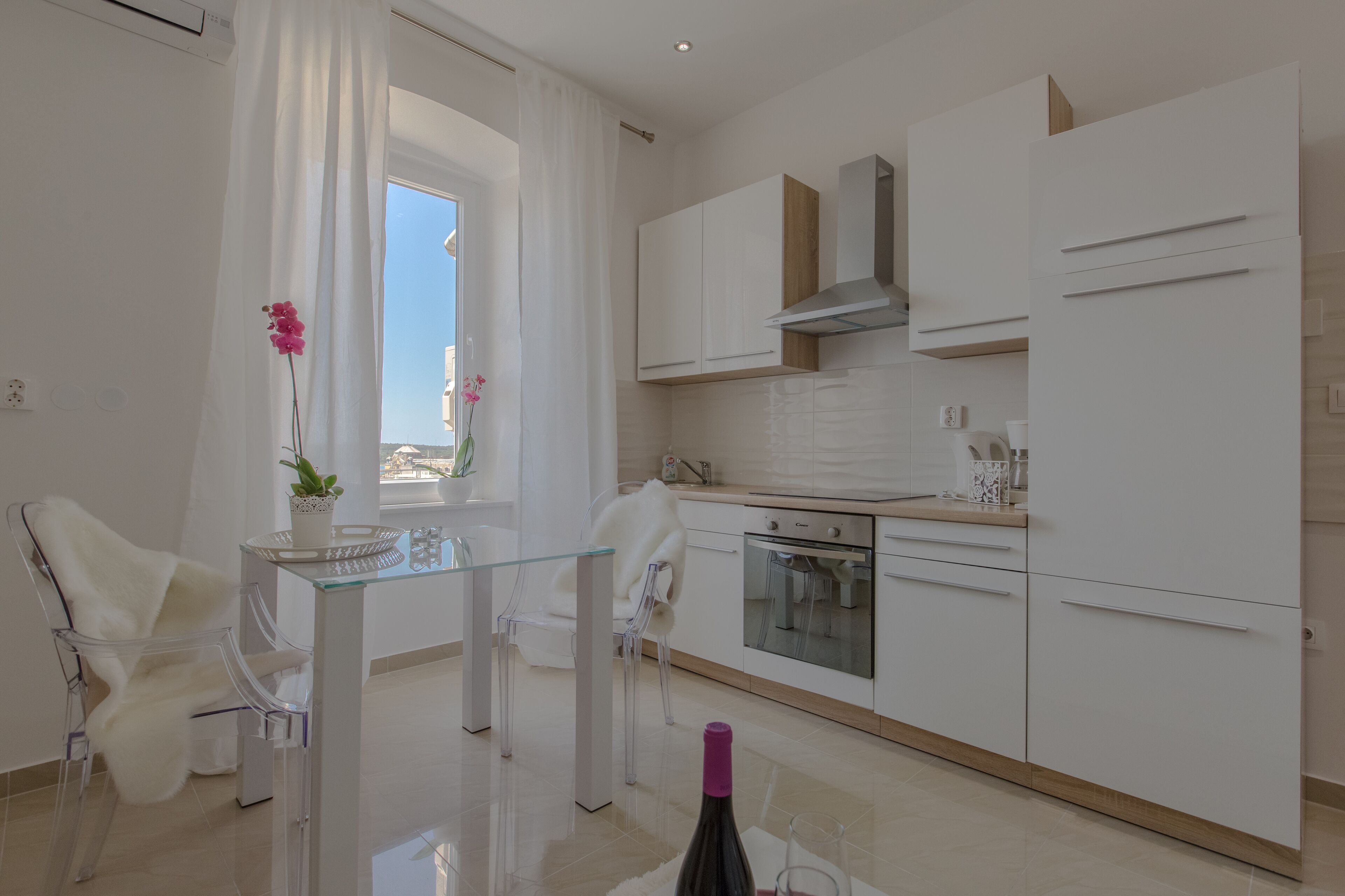 A modern kitchen with white cabinets, a stainless steel oven, and a glass dining table with chairs.