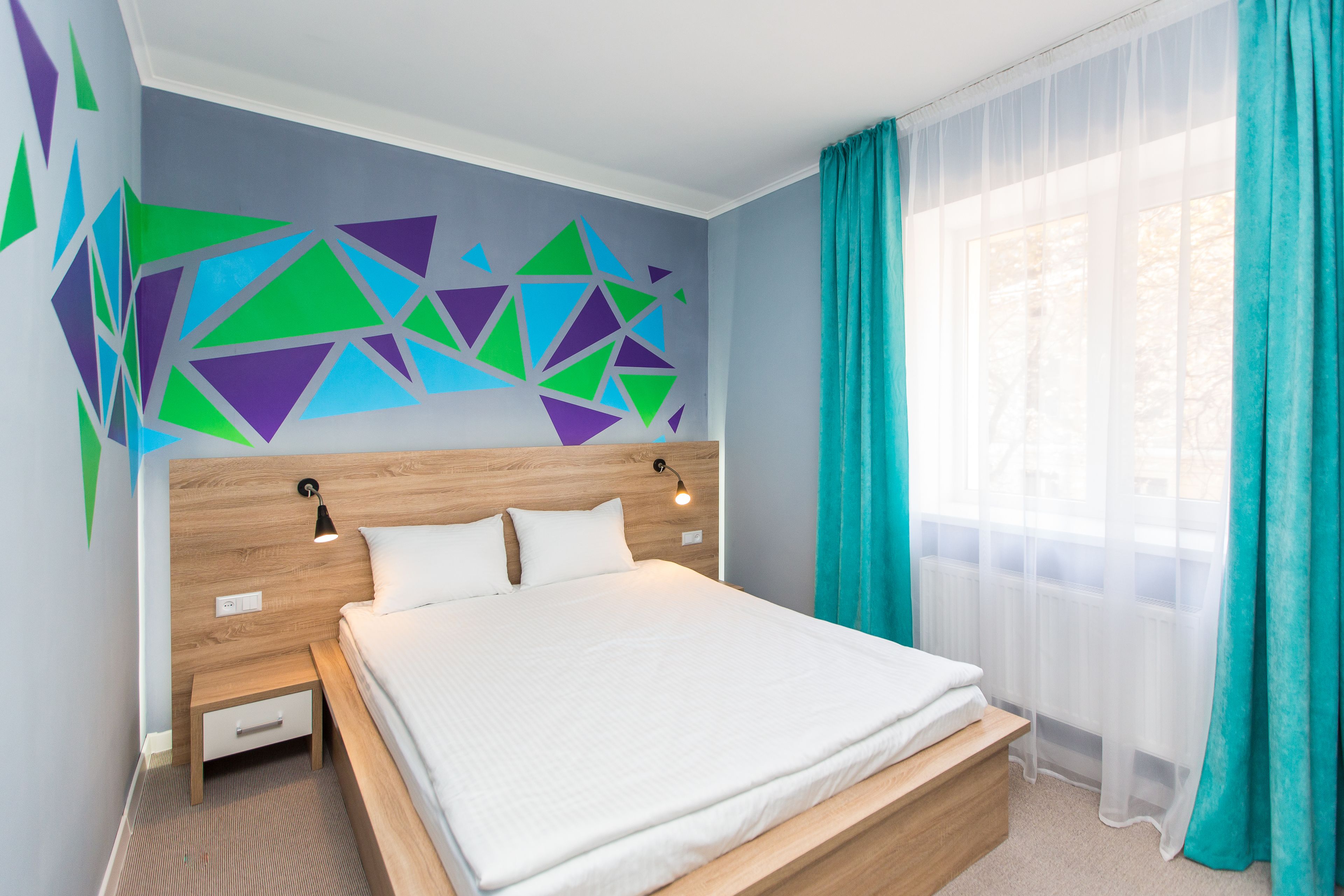 Une chambre à coucher moderne avec une tête de lit en bois, un grand lit, une table de chevet et un mur orné de motifs géométriques.