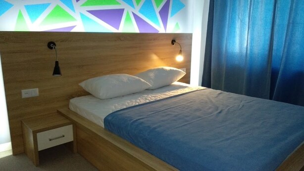 A bed with a wooden headboard, two bedside lamps, a nightstand with a drawer, and a blue blanket. - Blum Hotel (Lviv)
