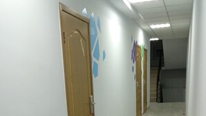 A long, narrow hallway with tiled flooring and white walls. There are several doors along the hallway, some with numbers above them. The hallway is well-lit with ceiling lights. - Blum Hotel (Lviv)