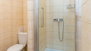 A glass-enclosed shower stall with a white toilet in a bathroom with beige tiles. - Blum Hotel (Lviv)
