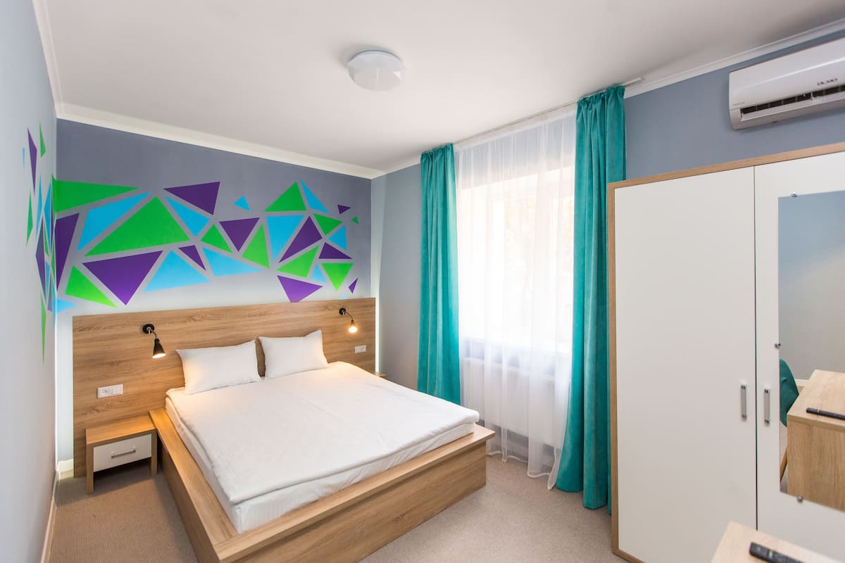 Une chambre d’hôtel moderne avec un lit en bois, une table de chevet, une lampe fixée au mur et une grande armoire.