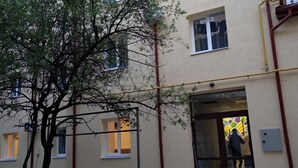 A building with multiple windows and a tree in front. There are visible pipes and a door leading to an interior space. - Blum Hotel (Lviv)