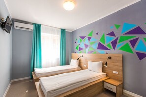 A hotel room with two single beds, a small bedside table with a lamp, a wall-mounted TV, and a window with curtains. - Blum Hotel (Lviv)
