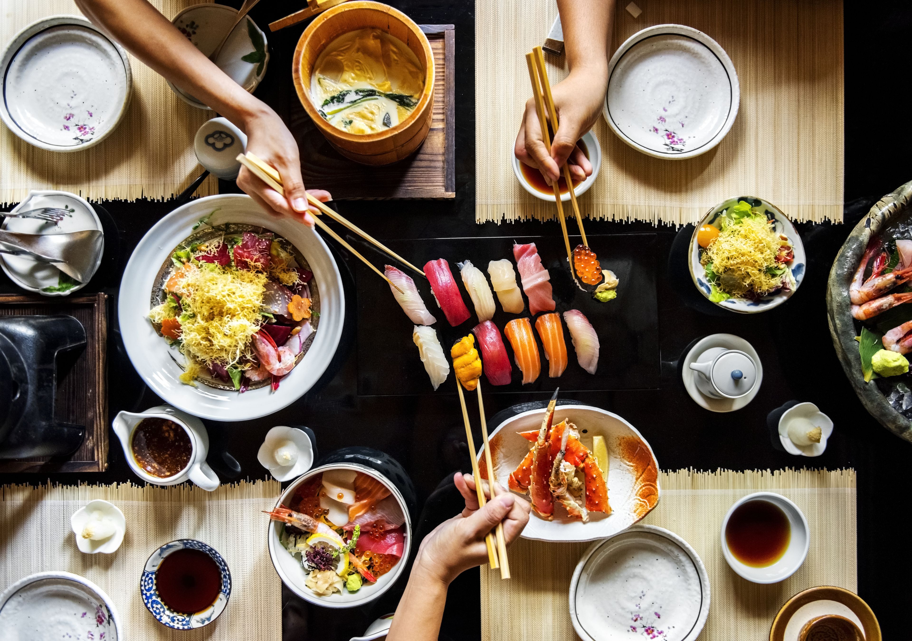Una mesa de comedor con diferentes platos, entre ellos sushi y sashimi, y varias fuentes de sopa.