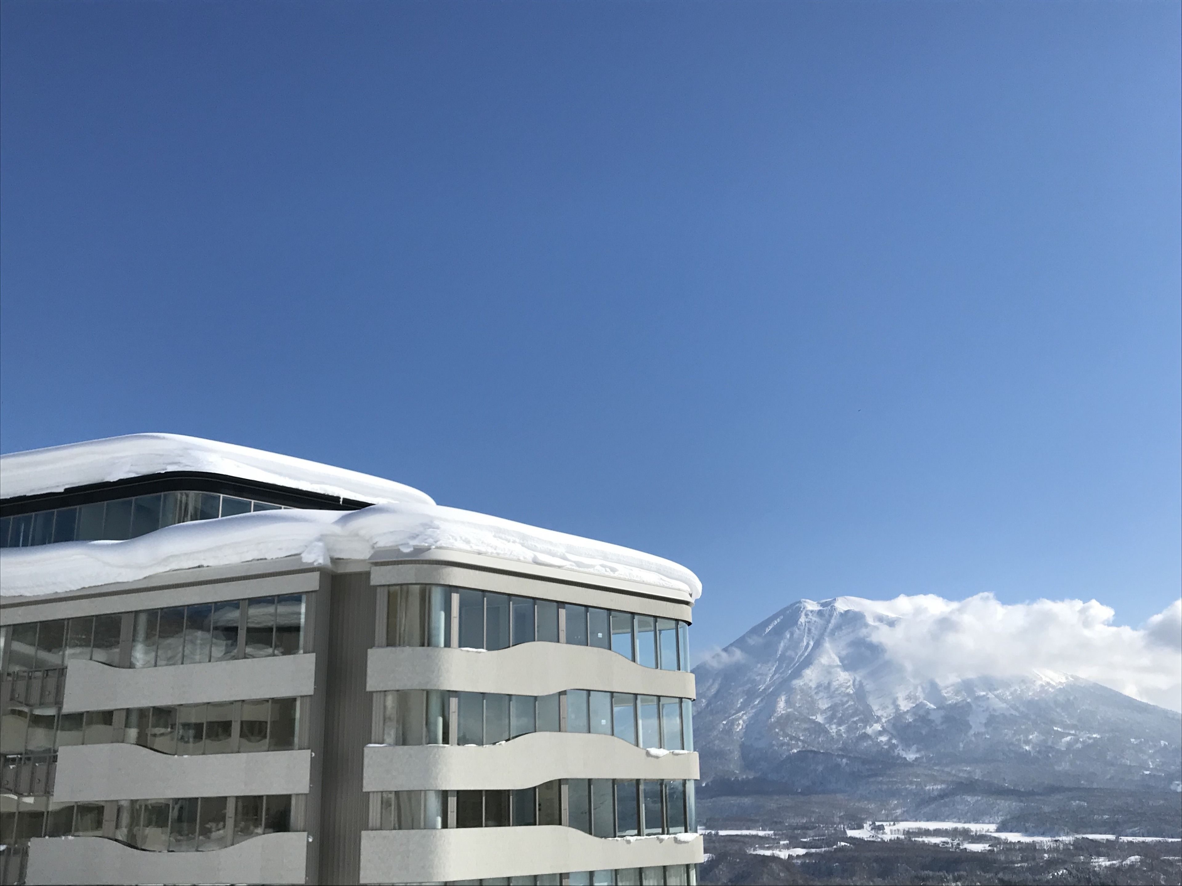 A modern building with multiple floors and large windows, covered in snow, with a mountain in the background.