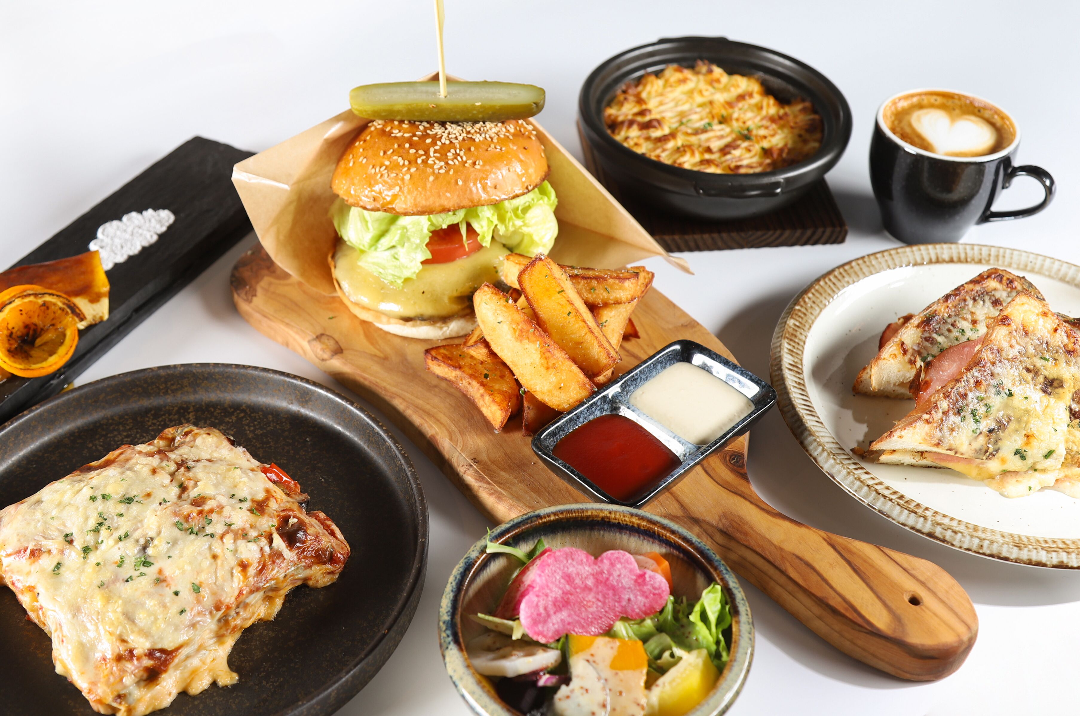 A variety of dishes including a burger, fries, a slice of pizza, and a steak, along with condiments and a cup of coffee.