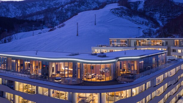A modern hotel with a glass facade, multiple levels, and a ski slope in the background. - Skye Niseko (Kutchan)