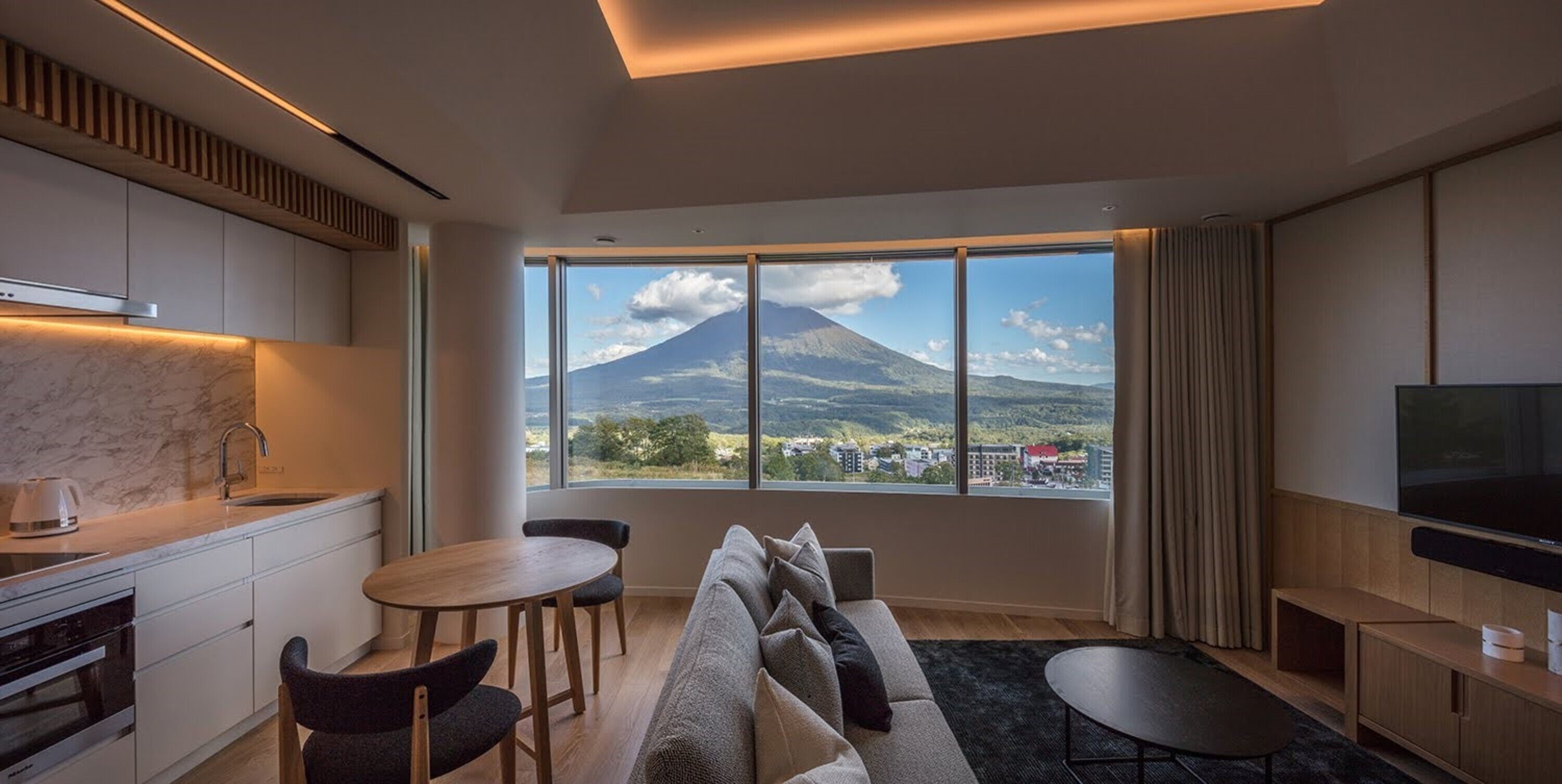Una sala de estar moderna con un ventanal grande, un sofá, una mesa de comedor y un televisor.