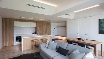 A modern kitchen with a central island, a dining area with a wooden table, and a grey sofa with cushions.
